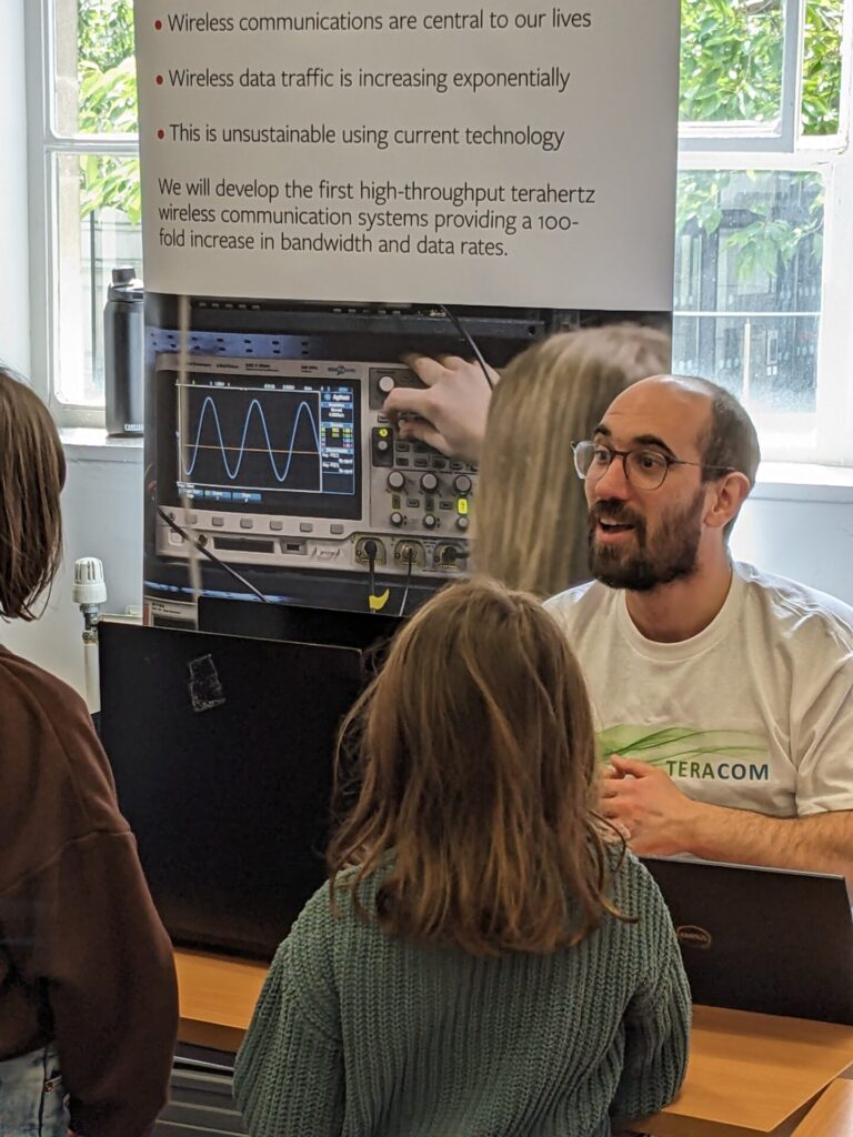 Photograph of researcher explaining the laser communications system to two children at the Be Curious family day 