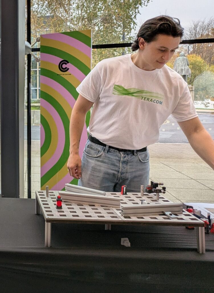 A TeraCom researcher in a 'TeraCom' t-shirt, with the laser maze demo in the foreground.