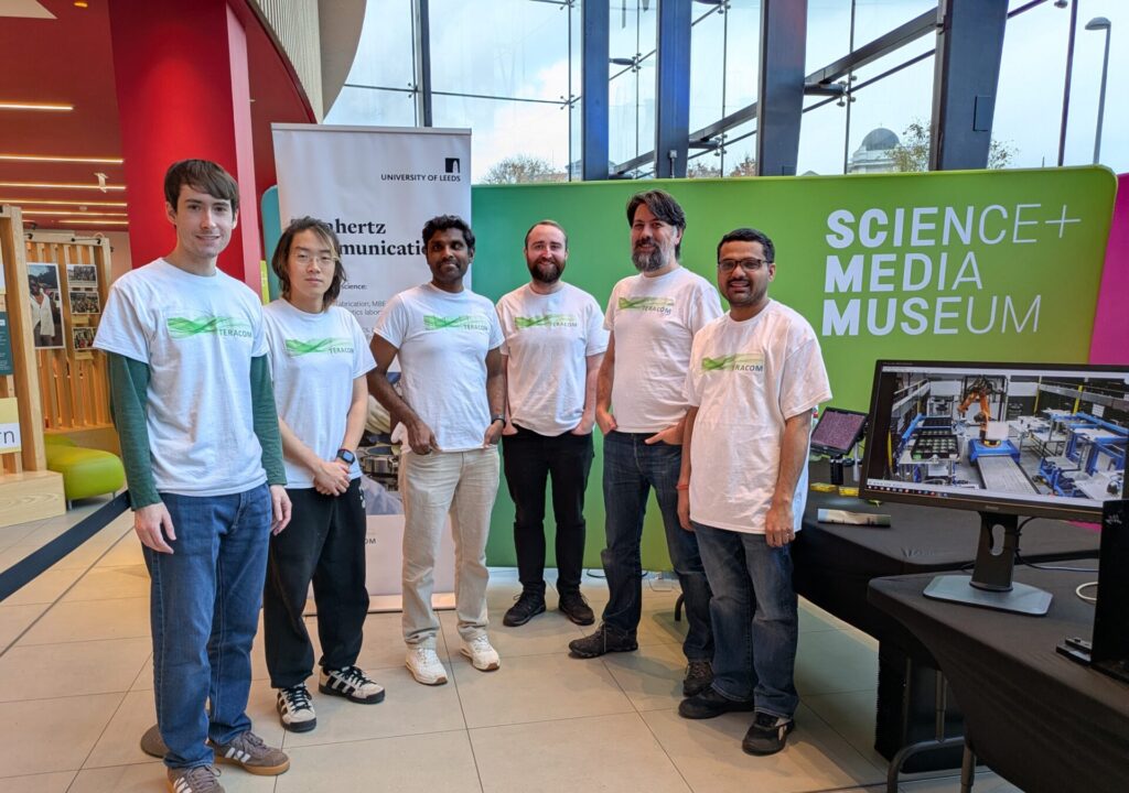 Six TeraCom researchers in 'TeraCom' t-shirts, stood in front of a sign saying 'Science + Media Museum'.