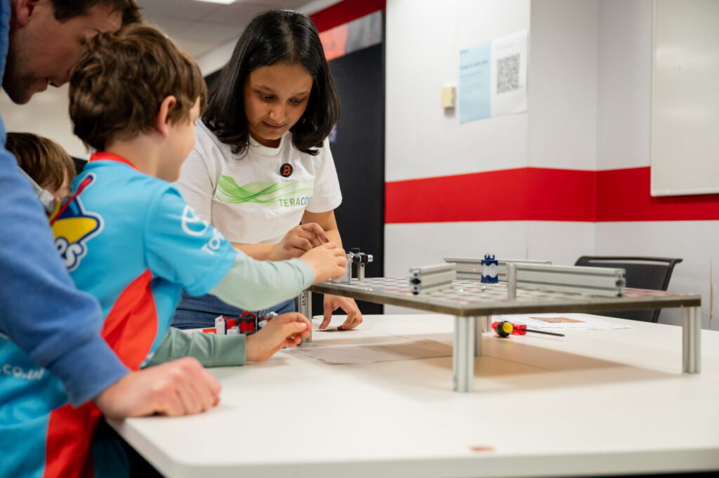 Sumona explaining how to complete the laser maze with a little boy at Be Curious 2026